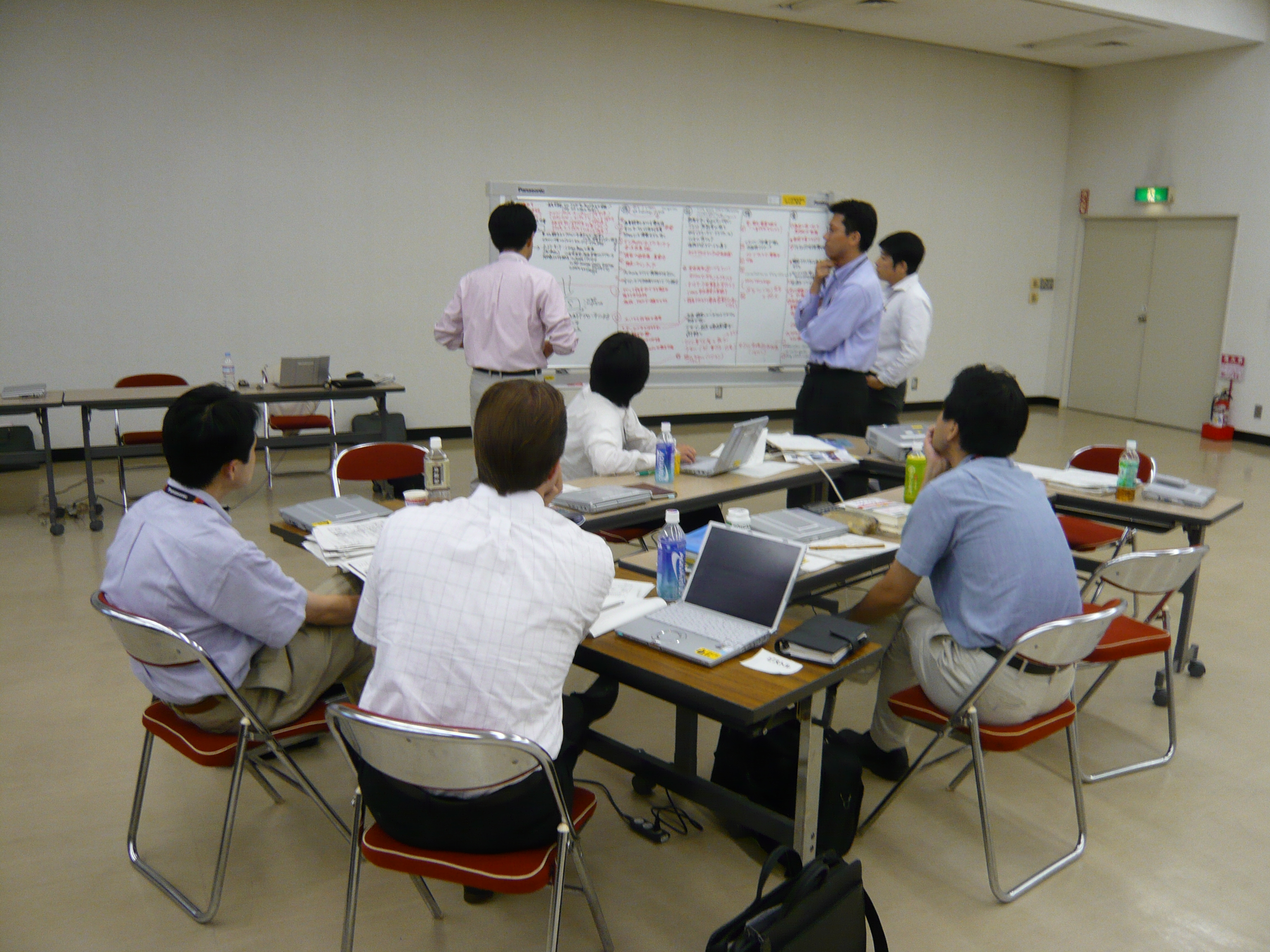 大きなホワイトボードを囲み、参加者が事業課題を検討するワークショップ